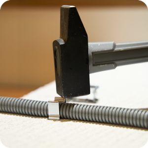 Hamer bevestigt kabelklem op golfbuis.