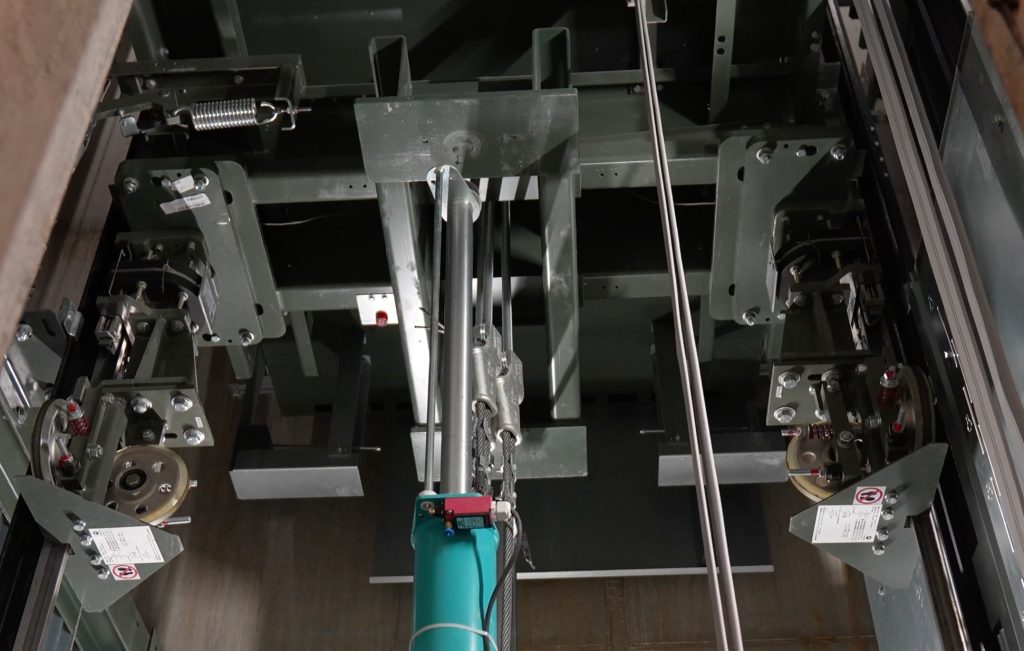 Interieur van een liftmachinekamer met kabels en wielen.