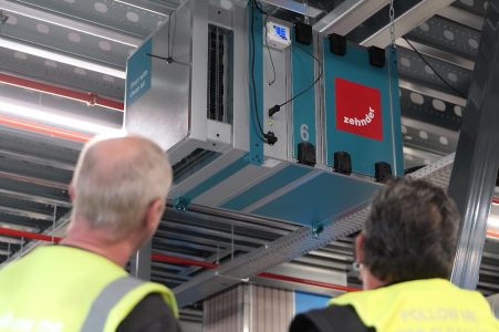 Ventilatiesysteem in bedrijfshal met mannen in veiligheidsvesten.