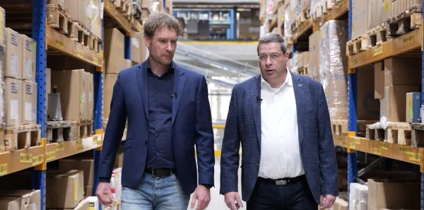 Twee mannen lopen door magazijn met dozen.